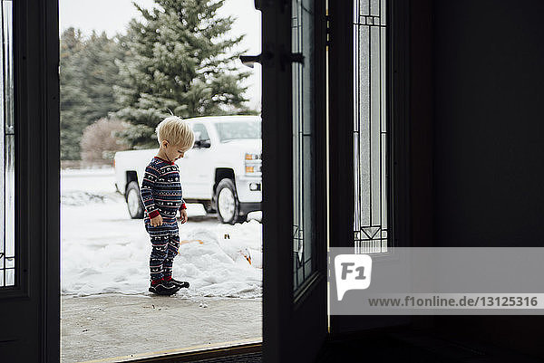 Seitenansicht des auf Schnee stehenden Jungen durch die Tür gesehen
