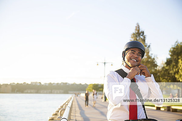 Happy businessman wearing cycling helmet while standing against sky