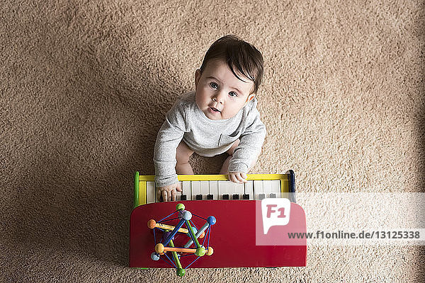Portrait eines süßen kleinen Jungen  der zu Hause auf einem Teppich Spielzeugklavier spielt