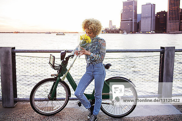 Frau riecht Blumenstrauss  während sie mit dem Fahrrad am Fluss steht