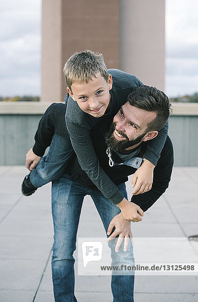 Glücklicher Vater nimmt Sohn huckepack  während er auf der Gebäudeterrasse steht