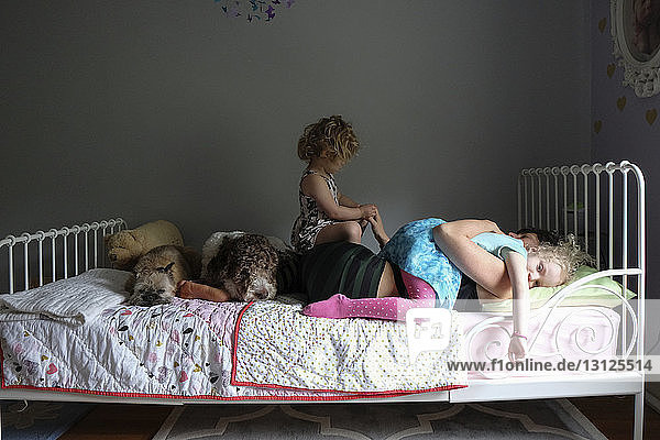 Töchter auf Mutter mit Hunden  die zu Hause im Bett an der Wand liegen