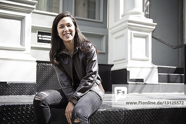 Portrait of happy young woman sitting on steps in city