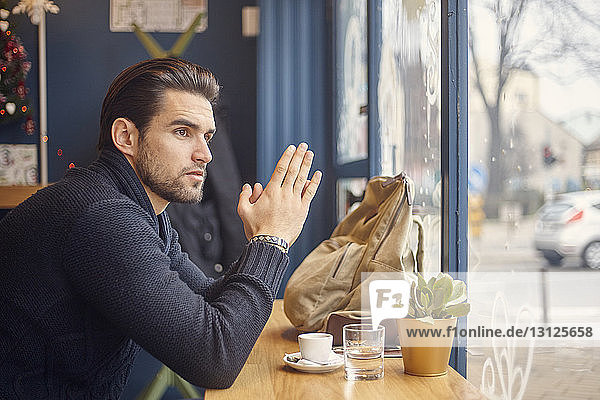Side view of man looking through window while sitting at cafe