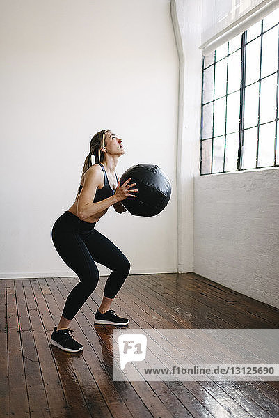 Female athlete carrying fitness ball while standing in gym