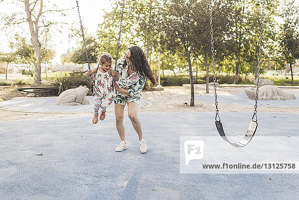 Glückliche Mutter schiebt Tochter auf Spielplatz schaukelnd
