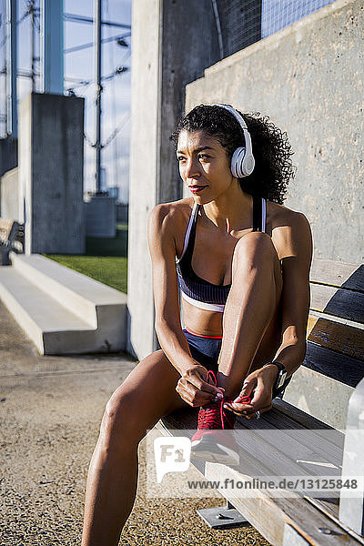 Weibliche Sportlerin bindet Schnürsenkel  während sie an einem sonnigen Tag auf einer Bank sitzt
