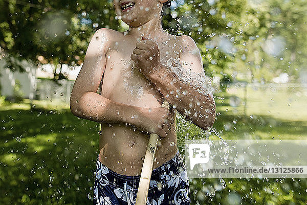 Mitschnitt eines glücklichen Jungen ohne Hemd  der im Garten mit Wasser spielt