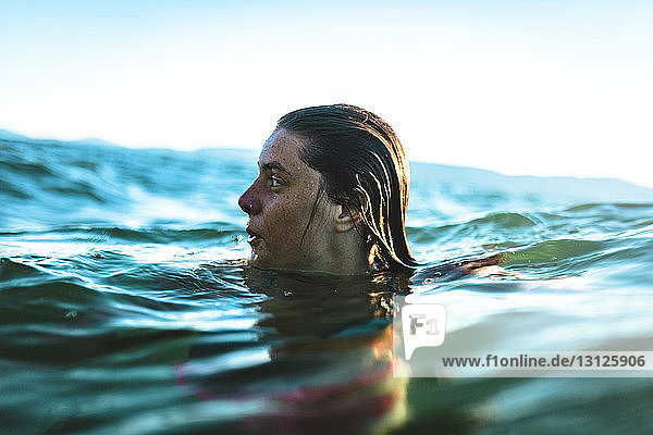 Woman looking away while swimming in sea against sky