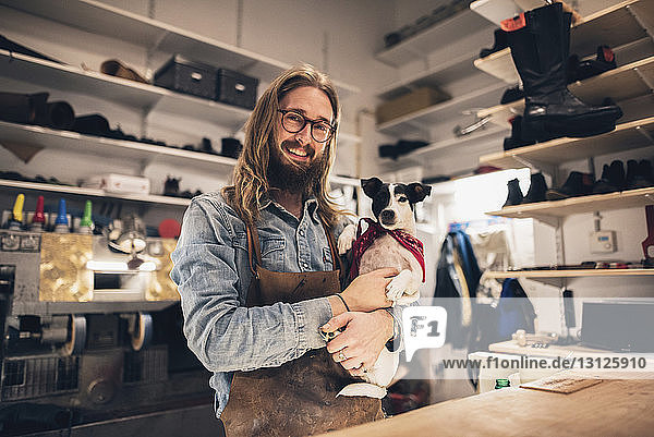 Portrait of smiling shoemaker carrying dog at workshop