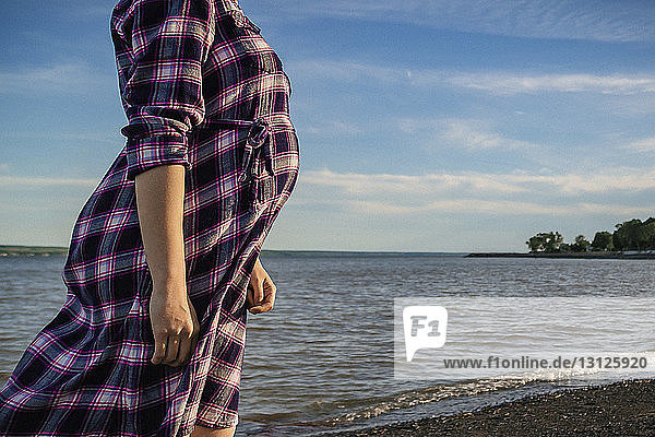 Midsection of pregnant woman standing on shore against sky