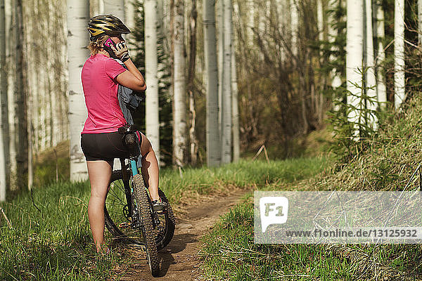 Sportlerin  die ein Mobiltelefon benutzt  während sie mit dem Fahrrad im Wald steht