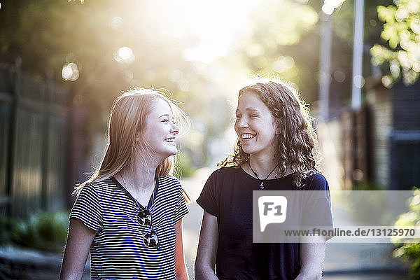 Happy sisters talking while standing on footpath