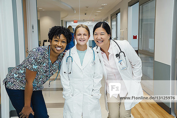 Portrait of cheerful female doctors with girl wearing lab coat in hospital corridor