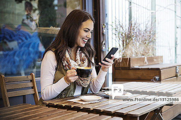 Smiling woman holding coffee cup while using mobile phone at cafe