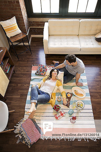 Hochwinkelansicht eines Paares  das sich beim Essen auf dem Teppich entspannt