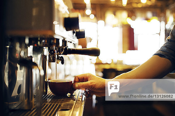 Abgetrennte Hand hält Kaffeetasse an Maschine