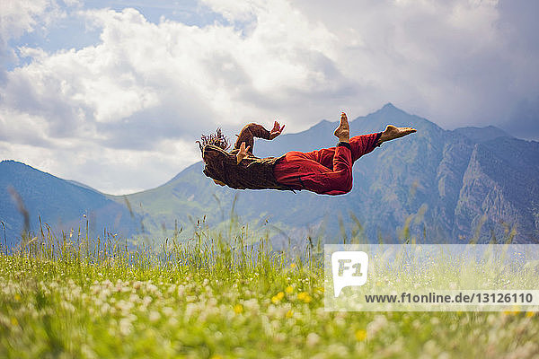 Frau in der Luft über Grasfeld gegen Berge