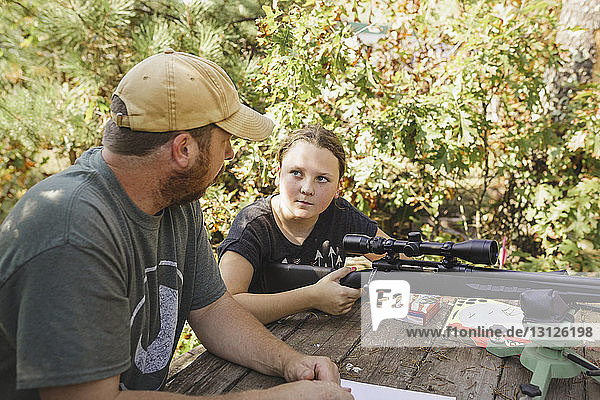 High angle view of daughter looking at father while holding rifle at backyard