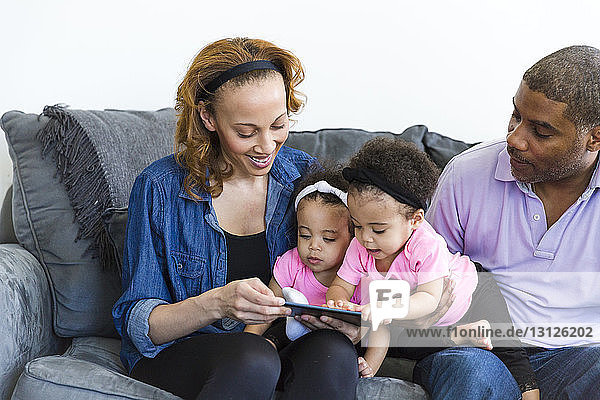 Eltern und Töchter schauen auf den Tablet-Computer  während sie auf dem Sofa sitzen