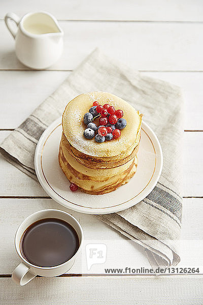 Schrägansicht von Pfannkuchen  die in Tellerform mit Kaffee und Milch auf Holztisch serviert werden