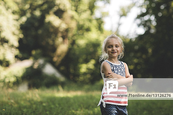 Bildnis eines lächelnden Mädchens mit verschränkten Armen auf Grasfeld stehend