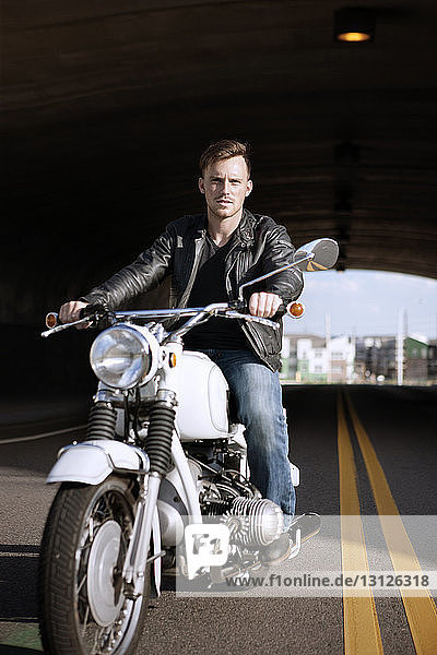 Portrait of biker riding motorcycle under bridge