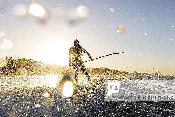 Surfer hält die Angelrute beim Surfen im Meer während des Sonnenuntergangs