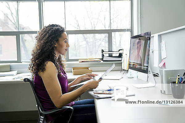 Seitenansicht einer Videokonferenz einer Geschäftsfrau mit einer Kollegin über einen Desktop-Computer im Büro
