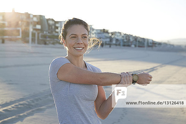 Lächelnde Frau streckt den Arm während eines sonnigen Tages am Strand
