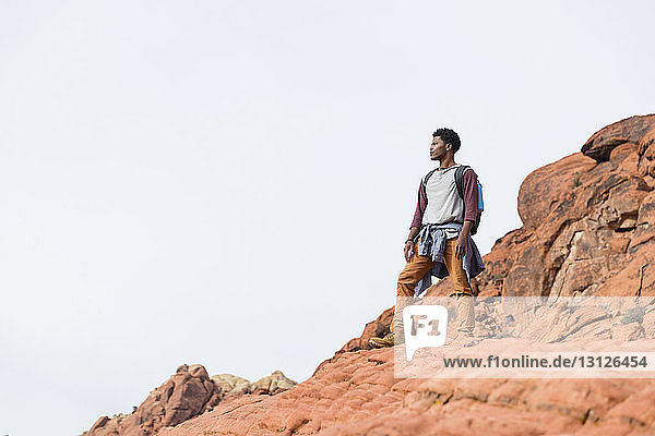 Niedrigwinkel-Ansicht eines Mannes  der weg schaut  während er auf einer Felsformation vor klarem Himmel steht