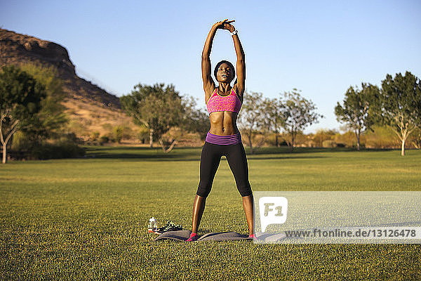 Woman practicing yoga on grassy field against clear sky