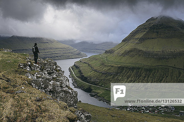 Wanderer schaut auf Aussicht  während er auf einer Klippe vor stürmischen Wolken steht