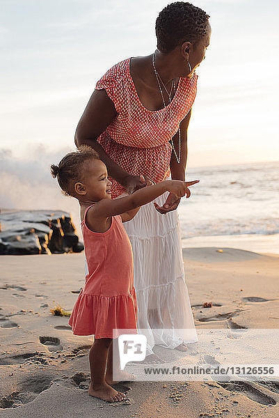 Mutter mit Tochter steht bei Sonnenuntergang am Strand gegen den Himmel