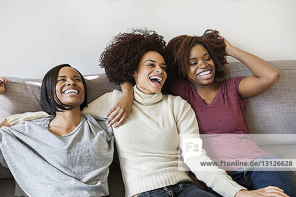 Cheerful female friends sitting on sofa at home