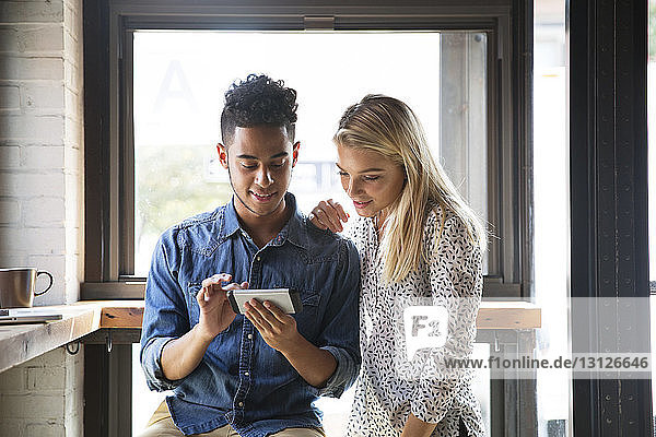 Smiling couple using mobile phone while sitting by window at cafe