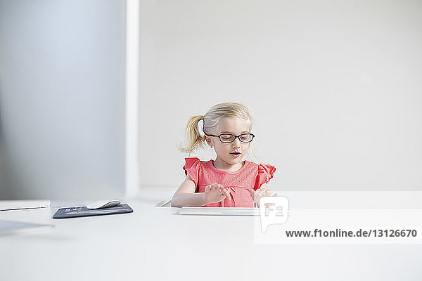 Happy girl wearing eyeglasses typing on keyboard at white table