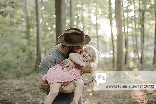 Vater mit Hut küsst Tochter  während er im Wald steht