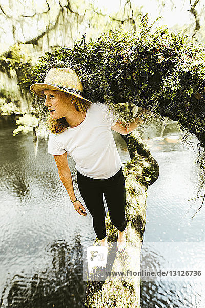 Young woman standing on mossy branch over lake at rainforest
