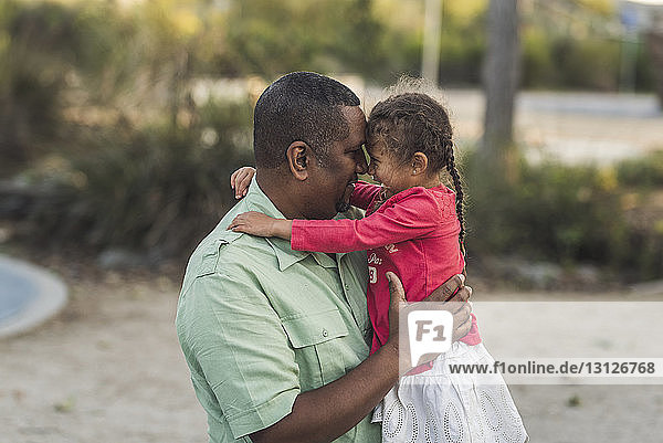Verspielter Vater und Tochter reiben sich auf dem Spielplatz die Nasen