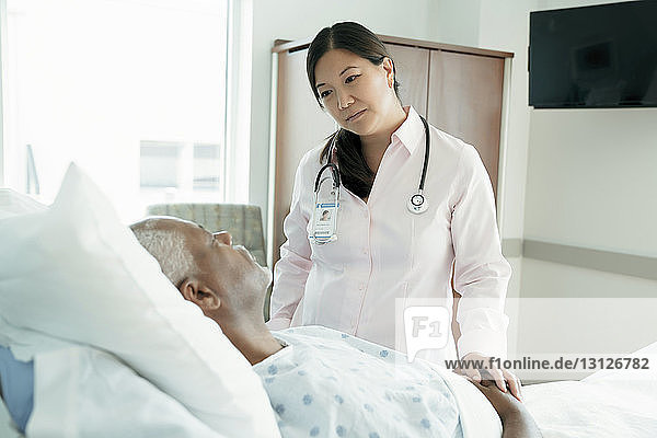 Female doctor looking at senior patient lying on bed in hospital ward