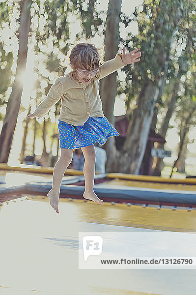 Mädchen springt auf dem Spielplatz in voller Länge auf dem Trampolin