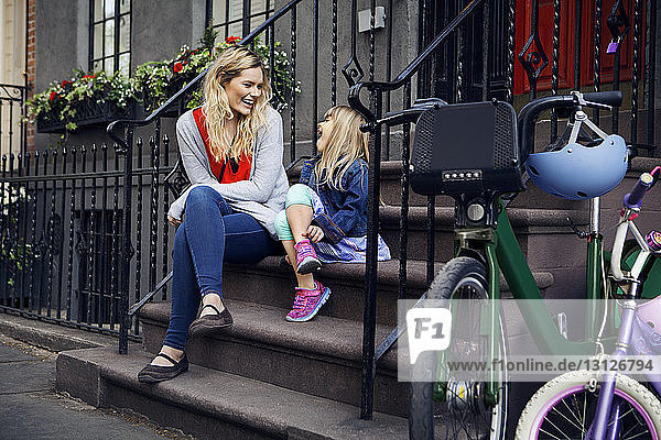 Glückliche Mutter und Tochter unterhalten sich im Sitzen auf Stufen