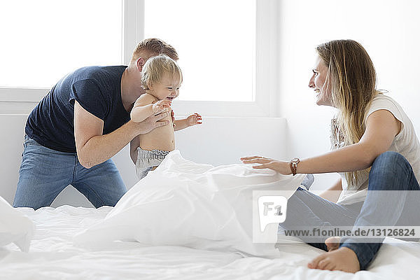 Glückliche Eltern spielen mit der Tochter im Bett