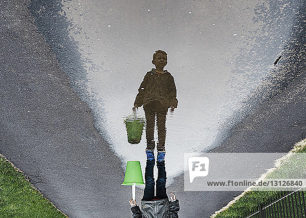 Auf dem Kopf stehendes Bild eines Jungen  der auf nasser Straße steht und einen Eimer trägt