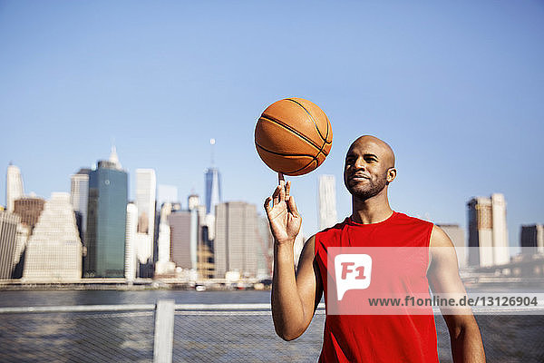 Lächelnder Mann dreht Basketball auf dem Finger gegen die Stadtsilhouette
