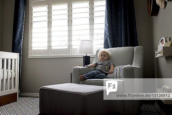 Junge in voller Länge  der sich auf einem Stuhl gegen das Fenster im Schlafzimmer ausruht