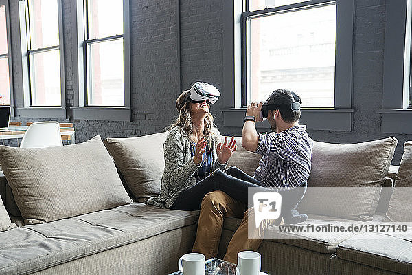 Glückliche Geschäftsleute tragen einen Virtual-Reality-Simulator  während sie im Büro auf dem Sofa sitzen