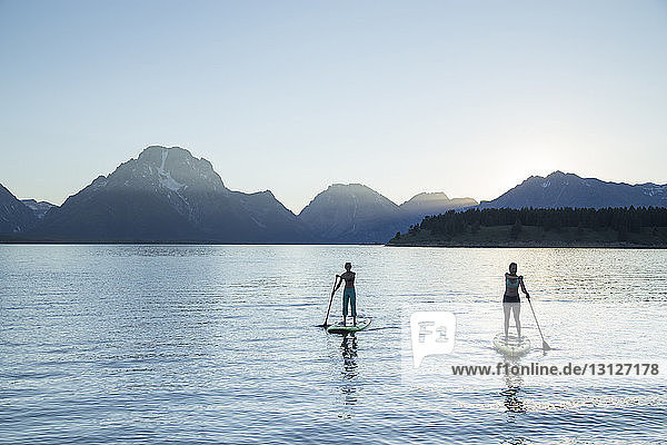Female friends paddleboarding on lake against clear sky at Grand Teton National Park