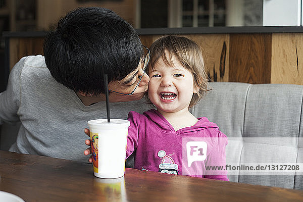 Father kissing happy daughter while sitting at table in cafe